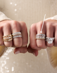 A close-up of a person's hands wearing multiple diamond rings from Memoire and Henri Daussi, featuring a cushion bezel band. Cushion bands set east-west in yellow gold and white gold