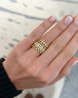 A close-up of a hand wearing a stack of three gold rings, each set with small clear stones, against a softly blurred light background.