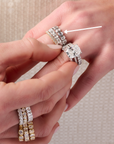 A close-up of a person's hands wearing multiple diamond rings from Memoire and Henri Daussi, featuring a cushion bezel band.