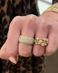 A close-up of a person's hand wearing two gold rings with pavé stones. One 3 row bezel set diamond band scattered round diamonds.