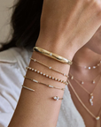 14k yellow gold cuff bracelet from Zoë Chicco features a single star-set diamond that totals 0.10ctw and at the center of the slim cuff. Shown and styled on a model's wrist stack.