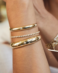 14k yellow gold cuff bracelet from Zoë Chicco features a single star-set diamond that totals 0.10ctw and at the center of the slim cuff. Shown and styled on a model's wrist stack.