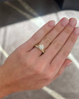 A close-up of a hand wearing a yellow gold ring with a round-cut diamond solitaire, paired with a yellow gold diamond band, set against a gray patterned background.