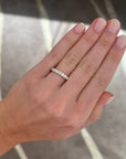 A close-up of a hand wearing a medium sized platinum band with round diamonds, set against a gray patterned carpet.