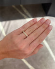 A close-up of a hand wearing a medium sized 1.02 carat yellow gold wedding band ring with round diamonds, set against a blurred gray and white marble-patterned background.