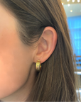 Gold hoop earring worn by a person with blurred background