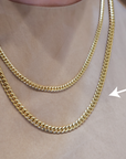 Two chains on a neck with the arrow pointing at the larger link chain.