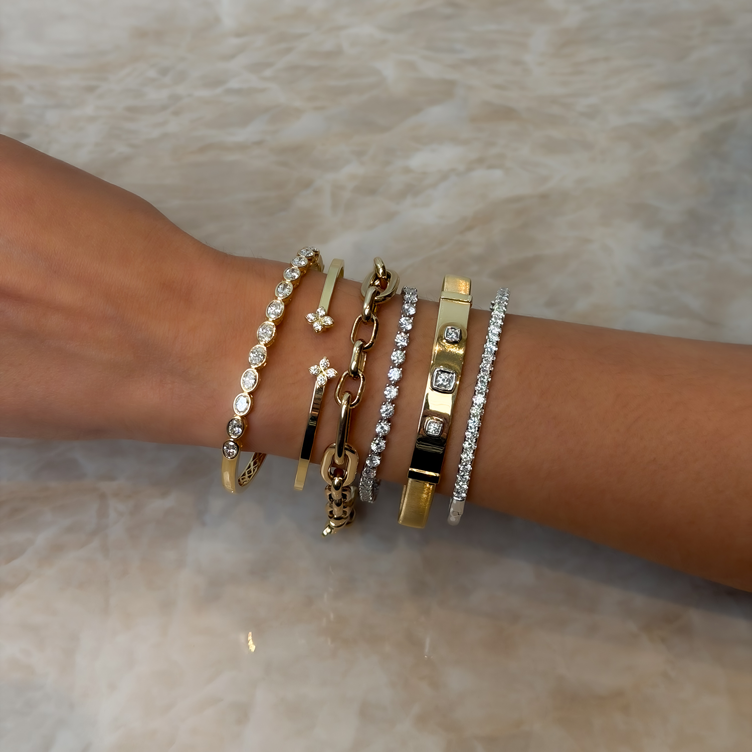 Stack of yellow gold and diamond bangles from designers Roberto Coin, Phillips House, Marco Bicego, and Brown & Co. featuring round diamonds, oval diamond, bezel set bangles, tennis bracelets, and paperclip chains