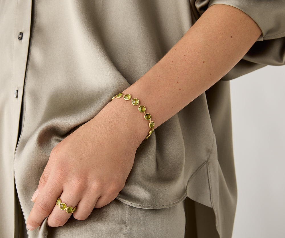 Yellow gold bracelet with bezel set peridot stones set in a line on a white background. displayed on a model.