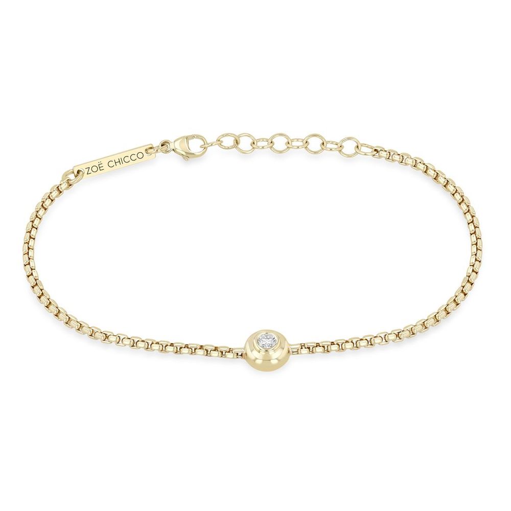 This 14k yellow gold bracelet from Zoe Chicco features a center bezel set diamond that totals 0.10ctw that is set on a box chain. The bracelet measures 6 inches in length with an adjustable chain extender. Shown on white background.