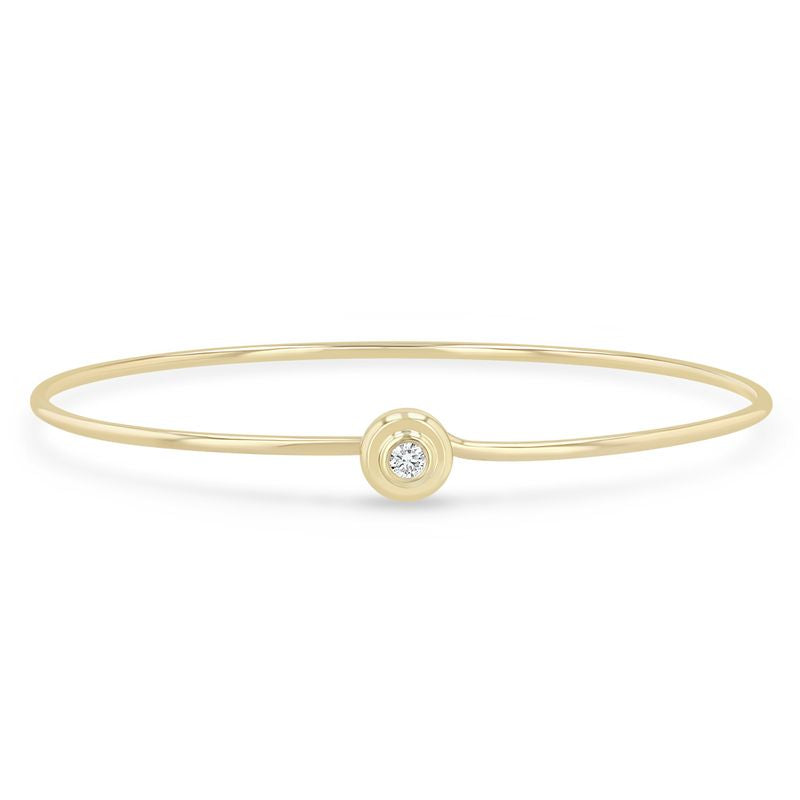 14k yellow gold bracelet from Zoe Chicco features a hard wire cuff design with an apron bezel set round diamond that measures 3mm in diameter and 0.10ctw. The bracelet hooks under the stone. Shown on a white background.