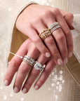 Close-up of two hands wearing multiple diamond rings, including stacked bands and a larger statement ring. All diamond bands from Brown & Co., Memoire, Henri Daussi. Featuring bezel set round & cushion diamonds in yellow gold and white gold. 