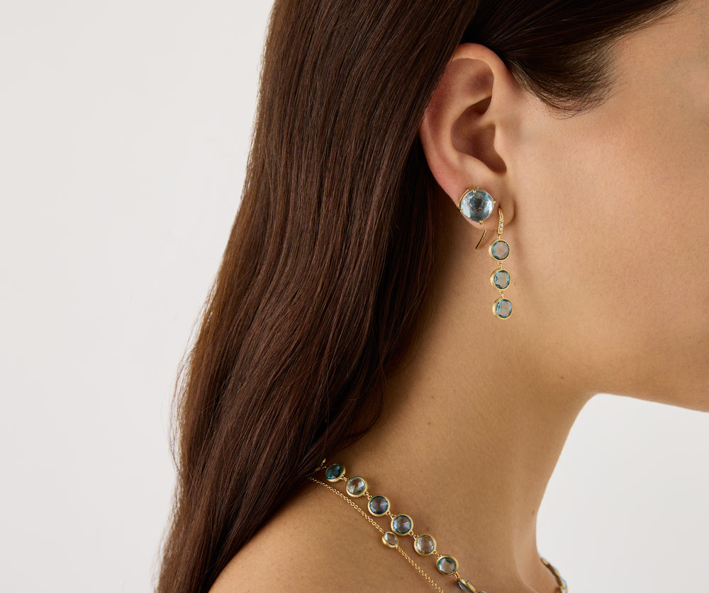 18K yellow gold drop earrings featuring bezel-set, rose-cut round blue topaz gemstones arranged in a continuous line with hook posts set with diamonds. Displayed on a model.