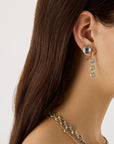 18K yellow gold drop earrings featuring bezel-set, rose-cut round blue topaz gemstones arranged in a continuous line with hook posts set with diamonds. Displayed on a model.