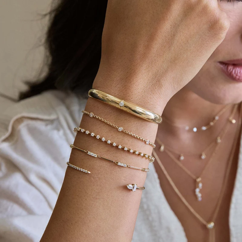 14k yellow gold cuff bracelet from Zoë Chicco features a single star-set diamond that totals 0.10ctw and at the center of the slim cuff. Shown and styled on a model's wrist stack.