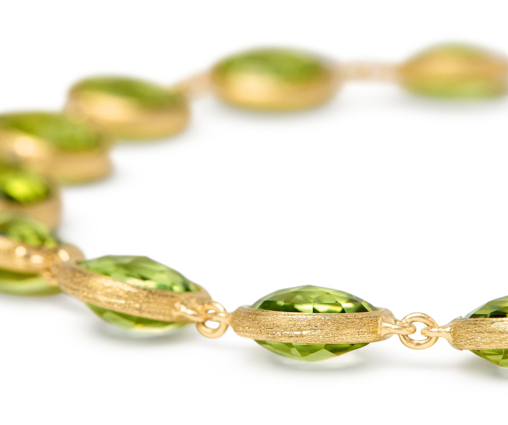 A close up shot of a Yellow gold bracelet with bezel set peridot stones set in a line on a white background.