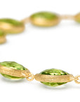 A close up shot of a Yellow gold bracelet with bezel set peridot stones set in a line on a white background.