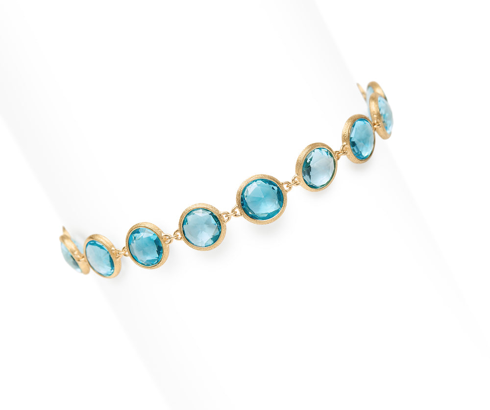Yellow gold bracelet with bezel set blue topaz stones set in a line on a white background.