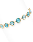 Yellow gold bracelet with bezel set blue topaz stones set in a line on a white background.