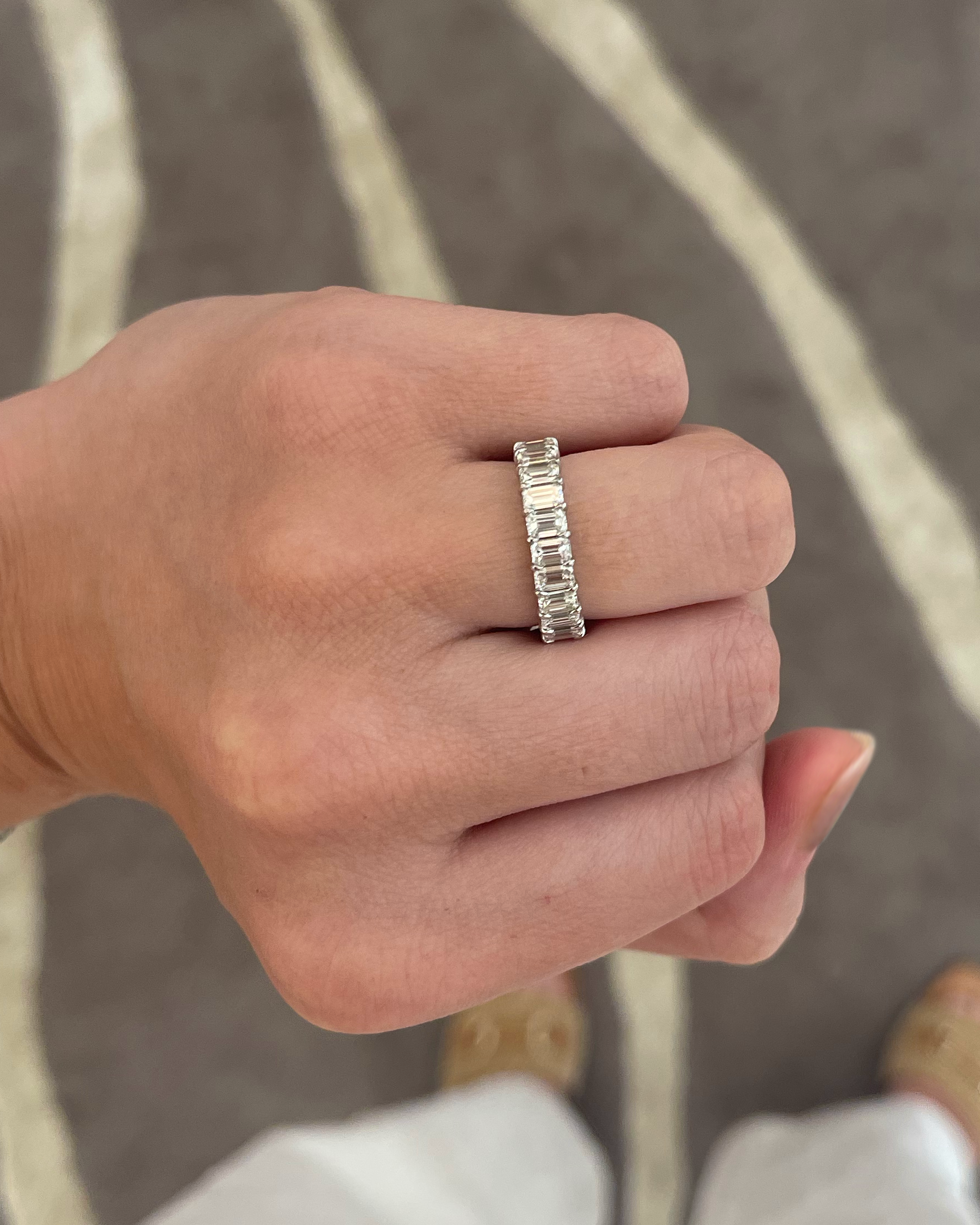 A close-up of a hand wearing a silver band ring with a textured, segmented design, set against a background of a gray patterned floor and white clothing.