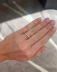 A close-up of a person's hand wearing a delicate gold band ring with round diamonds, set against a gray patterned background.