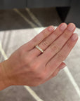A close-up of a person's hand wearing a large round diamond band ring, set against an indoor background with soft gray and beige tones