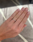 A close-up of a person's hand wearing a slim white gold diamond band ring set against a gray marble-patterned background.