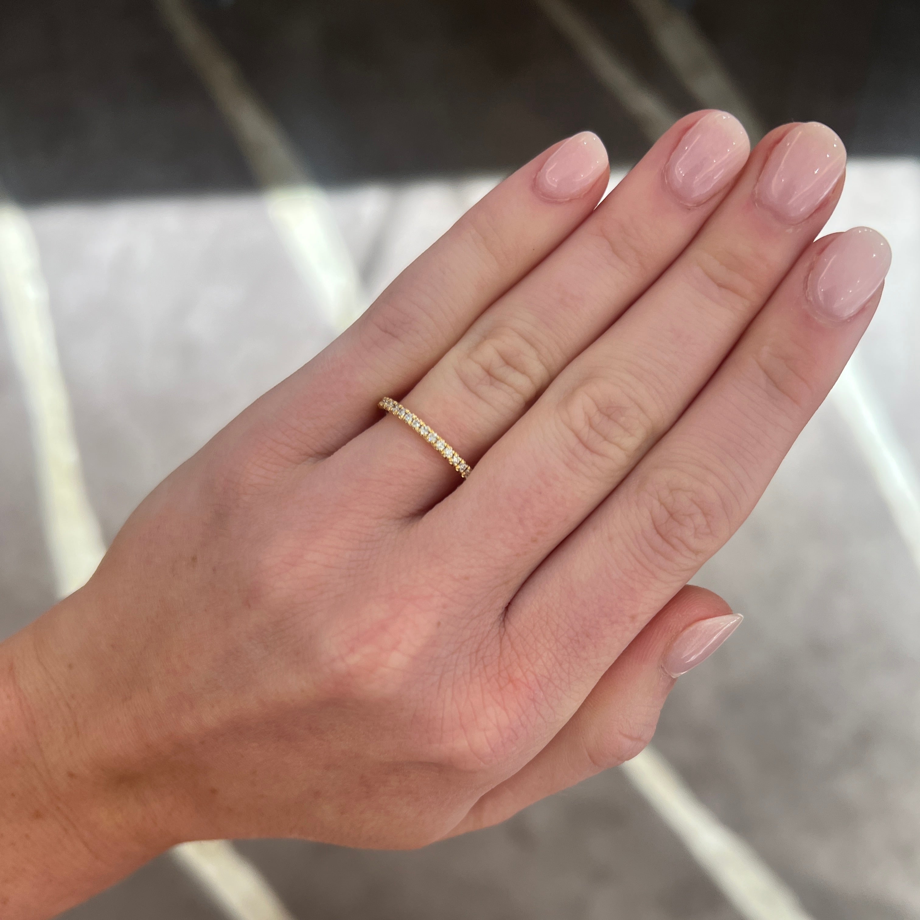 A close-up of a hand wearing a delicate yellow gold diamond band ring with small pavé-set stones