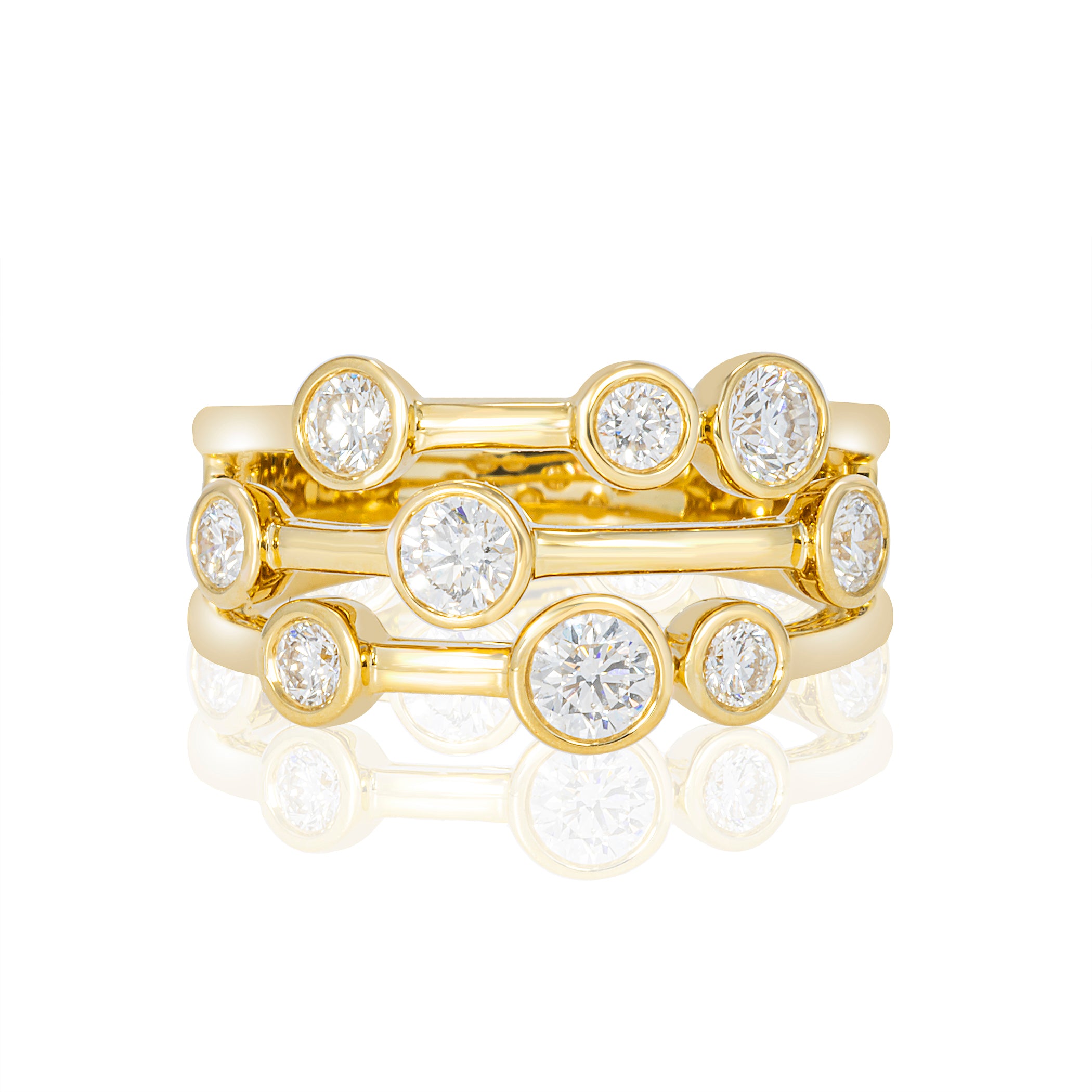 A yellow gold ring with three stacked bands, each featuring a round brilliant-cut diamond in a bezel setting, shown on a white background with a soft reflection.