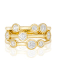 A yellow gold ring with three stacked bands, each featuring a round brilliant-cut diamond in a bezel setting, shown on a white background with a soft reflection.