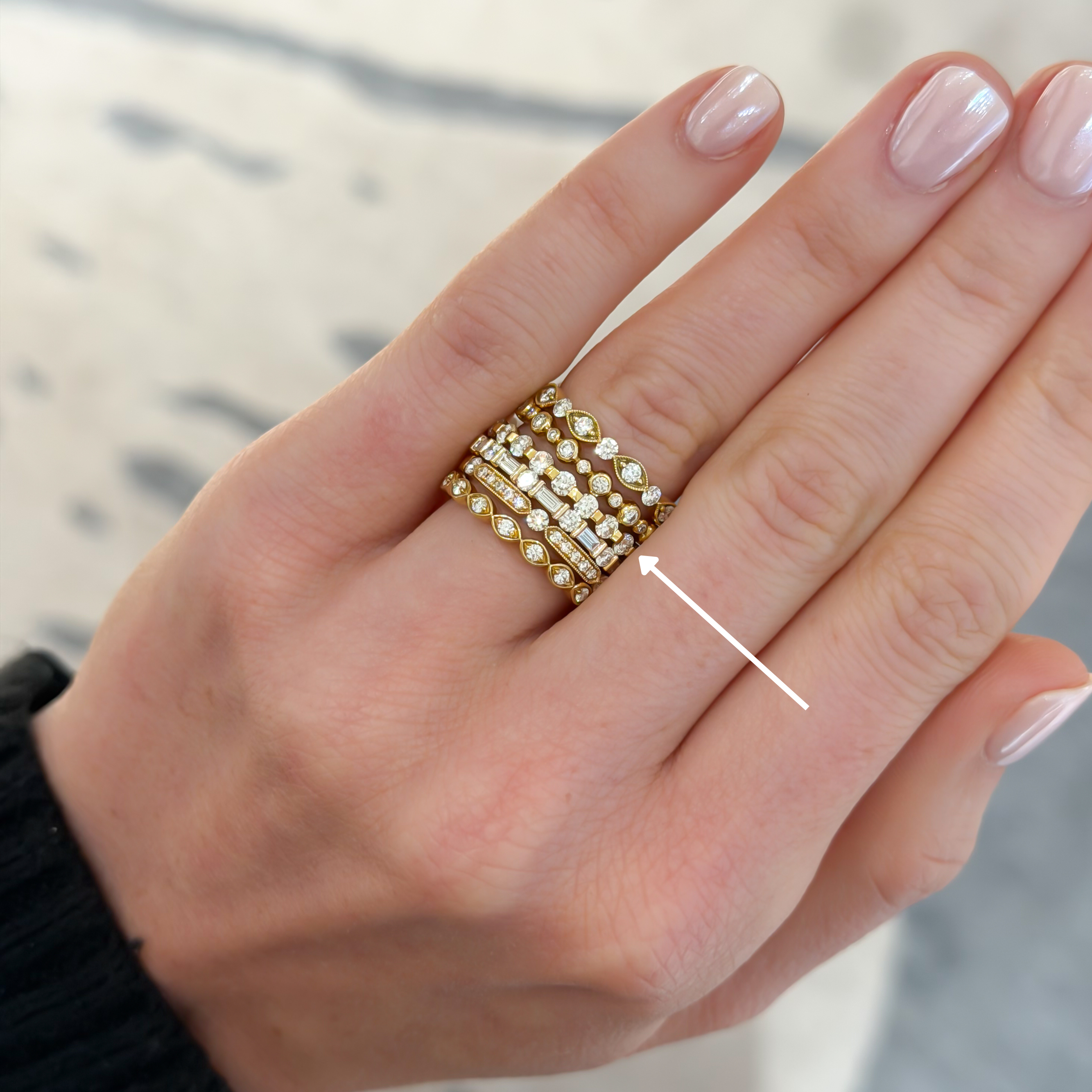 A close-up of a hand wearing a stack of multiple wedding bands from designers, Memoire, Henri Daussi, and Brown & Co., each set with diamonds. 