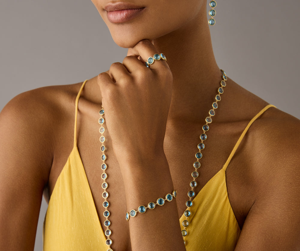 Yellow gold bracelet with bezel set blue topaz stones set in a line on a model.