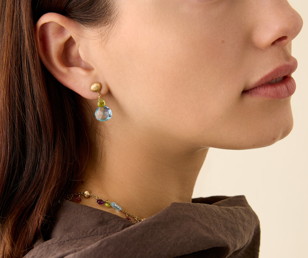 Yellow gold earrings with mixed gemstone drops from a hand engraved chain bead stud. On a model.