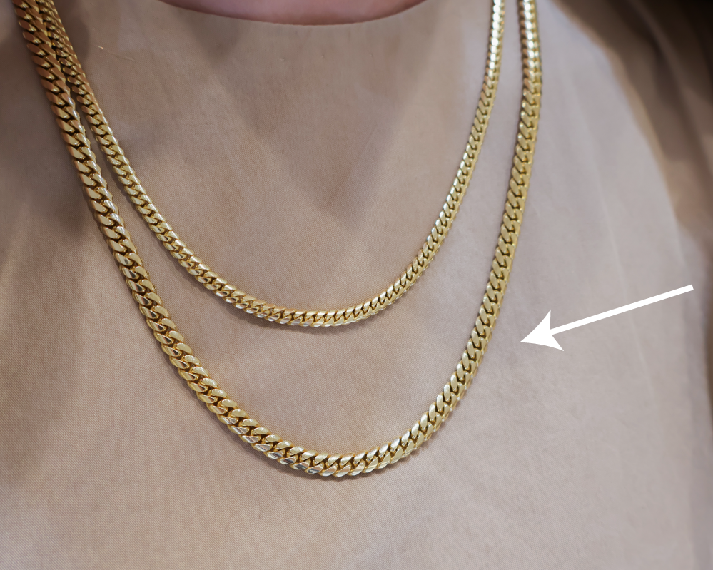 Two chains on a neck with the arrow pointing at the larger link chain.