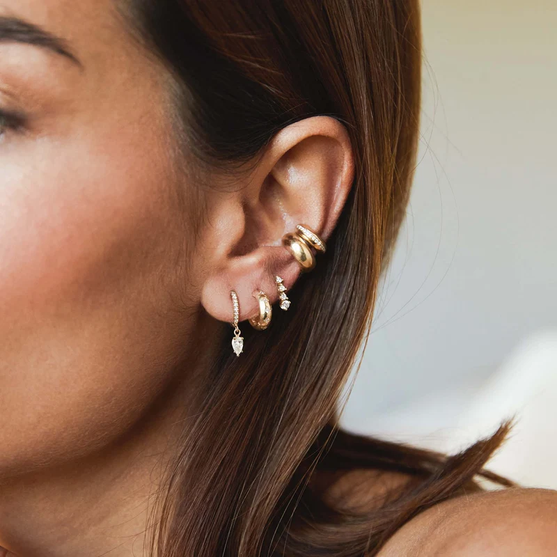 14k yellow gold huggie earrings from Zoe Chicco features five bead set diamonds that total 0.10ctw. Shown and styled on a model's ear stack.