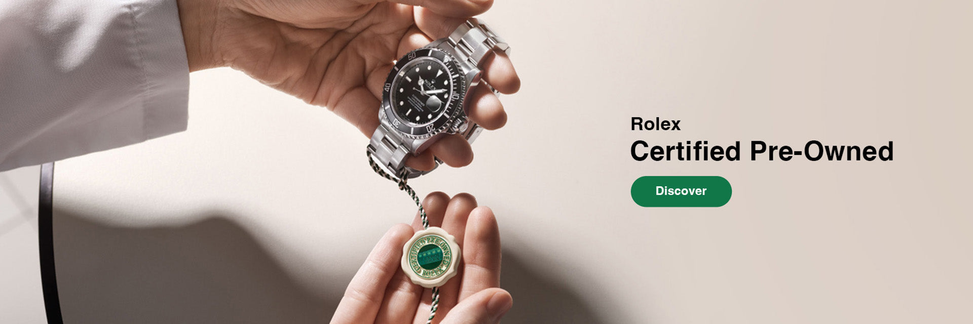 A person holds a silver-toned Rolex pre-owned watch and a small round green-and-white certificate in their hands against a clean light beige background, with text reading 'Rolex Certified Pre-Owned' and a green 'Discover' button on the right.